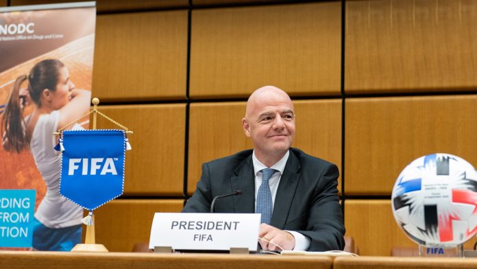 FIFA president Gianni Infantino sits at a press table behind a branded backdrop