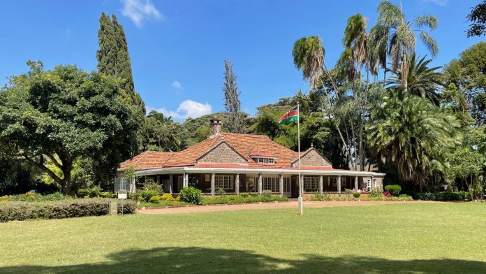 A low stone house with a tiled roof set behind a wide lawn and trees in Karen, Nairobi