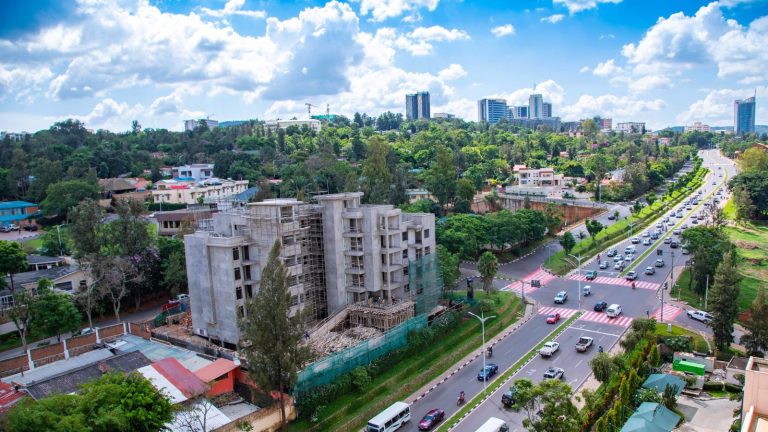 A wide street curving through central Kigali with hills and buildings behind