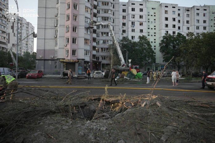 Rescue crews and a raised ladder platform beside a Kyiv apartment block with blown-out windows and a crater