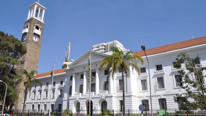 The white facade and clock tower of Nairobi City Hall behind palm trees