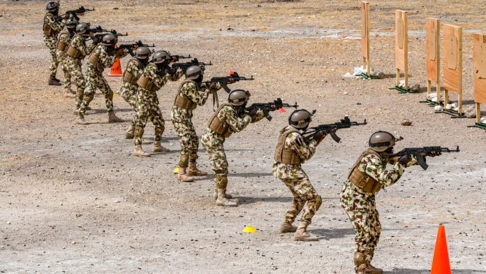 A line of Nigerian Army soldiers kneel and aim rifles during a live-fire exercise