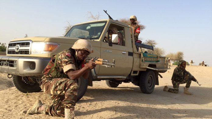 Nigerian Army soldiers take position beside a mounted patrol vehicle in open scrubland