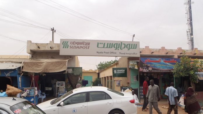 Shops, parked cars and pedestrians on a market street in Nyala, South Darfur