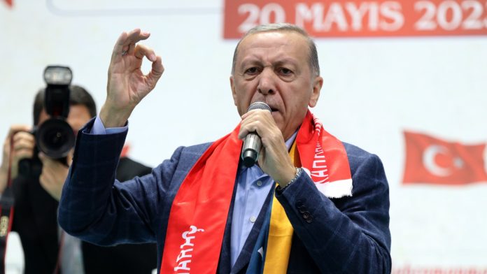 Turkish President Recep Tayyip Erdogan speaks into a microphone in front of national flags