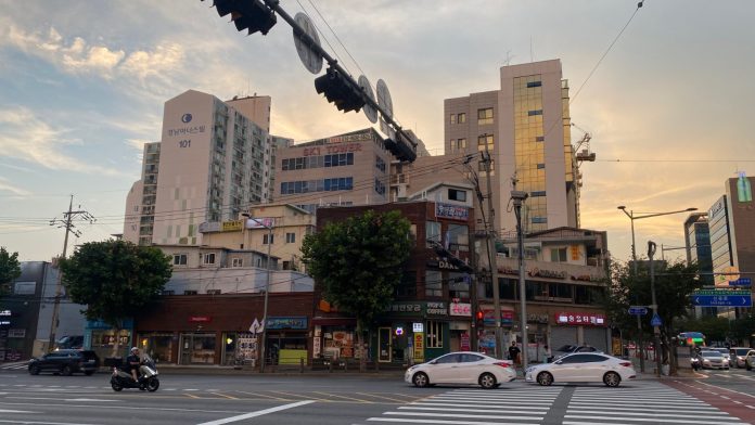 Cars and apartment blocks on a Seoul street under a hazy summer sky