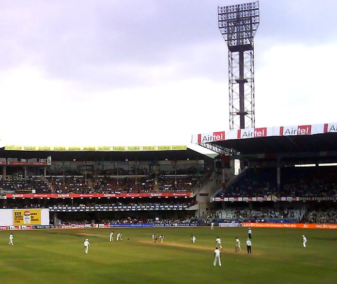 A Test cricket match in progress in front of a crowded stand